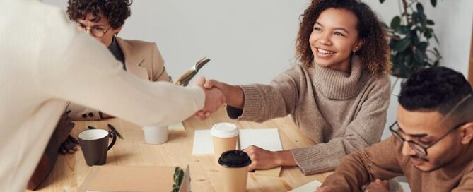 "Une jeune alternante est accueillie par un manager lors de son intégration en entreprise lors d'une réunion. Les collègues travaillent ensemble sur des ordinateurs portables, illustrant une collaboration efficace et une bonne intégration de l'alternant au sein de l'équipe."